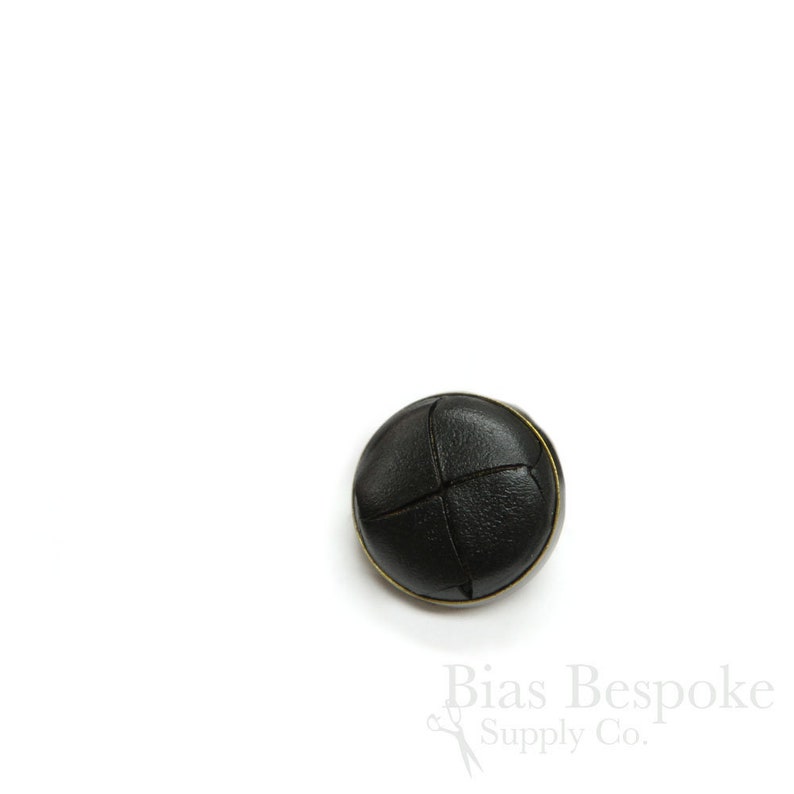May include: Black leather button with a stitched cross pattern and a gold metal rim.