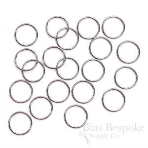 May include: A close-up of a pile of silver jump rings. The rings are all the same size and are scattered randomly on a white background.