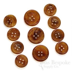 Puede incluir: Surtido de diez botones redondos marrones y tostados con cuatro agujeros cada uno. Los botones tienen un patrón moteado y están hechos de un material natural.