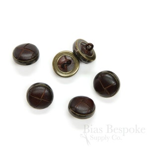 May include: Six brown leather buttons with a brass rim. The buttons have a cross-stitch pattern on the leather.