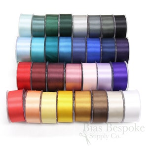 Puede incluir: Una colección de 24 carretes de cinta de satén en varios colores, incluyendo azul claro, verde azulado, burdeos, rosa, lavanda y blanco. Los carretes están dispuestos en filas, con el logotipo de Bias Bespoke Supply Co. visible en la parte inferior.