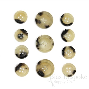 May include: Set of ten horn buttons in various sizes. The buttons are a light beige color with dark brown mottled patterns. The buttons have four holes each.