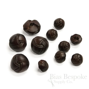May include: A collection of 10 brown leather buttons with a knotted design. The buttons are various sizes and are arranged on a white background.