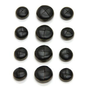 May include: Assortment of ten black leather buttons with gold stitching. The buttons are round and have a slightly raised center. They are arranged in three rows on a white background.