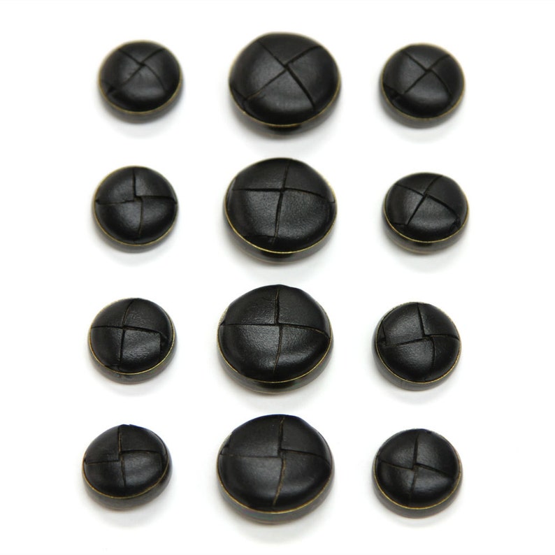 May include: Assortment of ten black leather buttons with gold stitching. The buttons are round and have a slightly raised center. They are arranged in three rows on a white background.