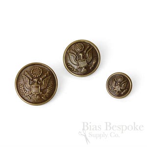 May include: Three antique brass buttons featuring the Great Seal of the United States. The buttons vary in size and depict an eagle with outstretched wings, olive branches, and arrows. The buttons are on a white background.