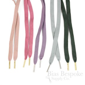 May include: Assorted colored shoelaces with metal aglets. The laces are in shades of pink, purple, gray, and green. The aglets are gold and silver. The text "Bias Bespoke Supply Co." is visible in the bottom right corner.