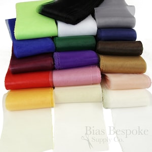 May include: A stack of 16 rolls of sheer ribbon in various colors, including green, blue, red, purple, pink, yellow, white, and black. The ribbon is arranged in a rainbow pattern. The ribbon is 1 inch wide and is made of a soft, lightweight fabric. Bias Bespoke Supply Co. is printed on the bottom of the image.