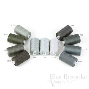 Pode incluir: Uma coleção de carretéis de linha em vários tons de cinza, verde e castanho, dispostos sobre um fundo branco. Cada carretel é rotulado com um número. A imagem inclui o texto "Bias Bespoke Supply Co."
