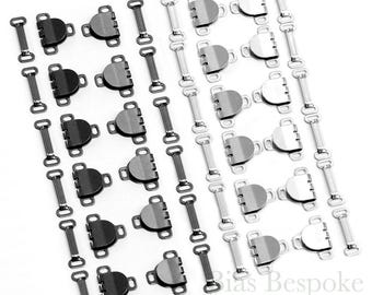 May include: A set of 24 black and silver hook and eye closures. The closures are arranged in two rows, with the black closures on the left and the silver closures on the right. The closures are all the same size and shape, and they are designed to be used for sewing.