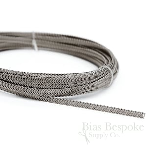 May include: A roll of silver chainmail trim, a type of decorative trim used for clothing and accessories. The chainmail is made of small, interlocking metal rings.