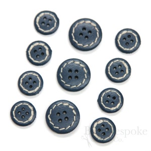 May include: Assortment of ten navy blue leather buttons with white stitching. The buttons have four holes each and vary in size.