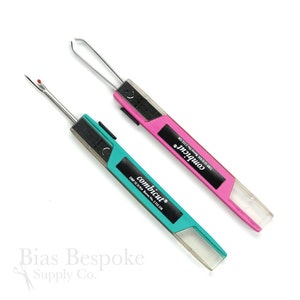 May include: Two sewing tools, one pink and one teal, with a clear plastic handle and a metal blade. The tools are labeled "combicut" and have the text "DBP 32 31 334 Brevet No. 2532 338".