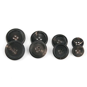 May include: Set of six black and brown round buttons with five holes each. The buttons are made of a natural material, possibly coconut shell.