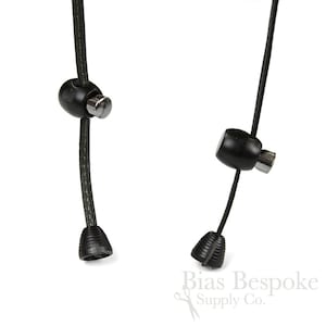 May include: Two black cord ends with metal tips and black plastic stoppers. The cord ends are attached to a black cord.