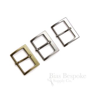 May include: Three metal belt buckles in different finishes: gold, silver, and nickel. The buckles are rectangular with a smooth, polished surface.