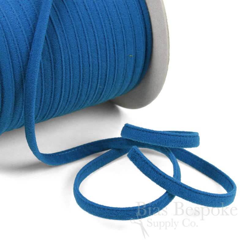 May include: A spool of teal blue elastic cord with a soft, velvety texture. The cord is wound around a cardboard spool and is ready to be used for sewing or crafting projects.