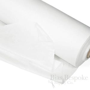 Puede incluir: Un rollo de tela de entretela blanca. La tela es un material ligero no tejido que se utiliza para estabilizar y dar rigidez a las telas.