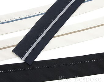 May include: Close-up of several bias tape strips in various colors. The strips include navy blue, black, and off-white, each with a contrasting stripe and decorative stitching. The Bias Bespoke Supply Co. logo is visible in the bottom right corner.