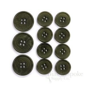 May include: An assortment of olive green buttons in various sizes, each with four holes. The buttons have a subtle wood grain texture and are arranged on a white background. The buttons are suitable for sewing and craft projects.