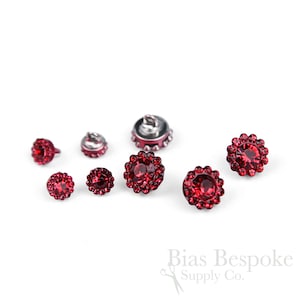 May include: Assortment of red rhinestone buttons in various sizes. The buttons have a silver metal base and are surrounded by a circle of red rhinestones.