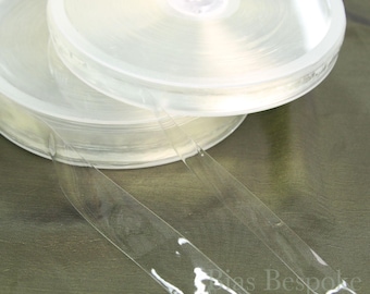 May include: Two rolls of clear, transparent bias tape are stacked on top of each other. The tape is unwound from the rolls, with two strips extending towards the bottom of the image. The rolls are in a clear plastic container.