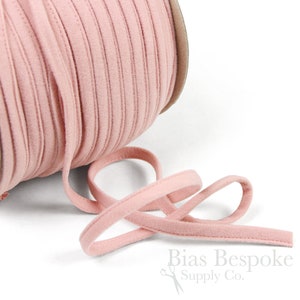 May include: A spool of pink bias tape, a type of fabric trim, with a length of tape extending from the spool. The tape is soft and has a slightly textured surface.