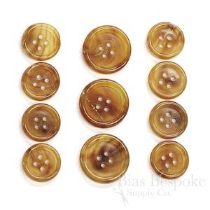 May include: Set of ten brown horn buttons, each with four holes. The buttons are arranged in three rows, with the largest buttons at the top and the smallest buttons at the bottom.