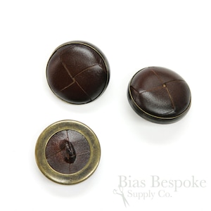 May include: Three brown leather buttons with a brass rim. The buttons have a woven design.
