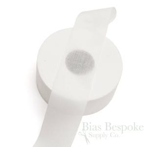 May include: A white roll of bias tape, a type of fabric used for finishing edges of garments, is shown on a white background. The tape is rolled up and a small section is unrolled, showing the white fabric.