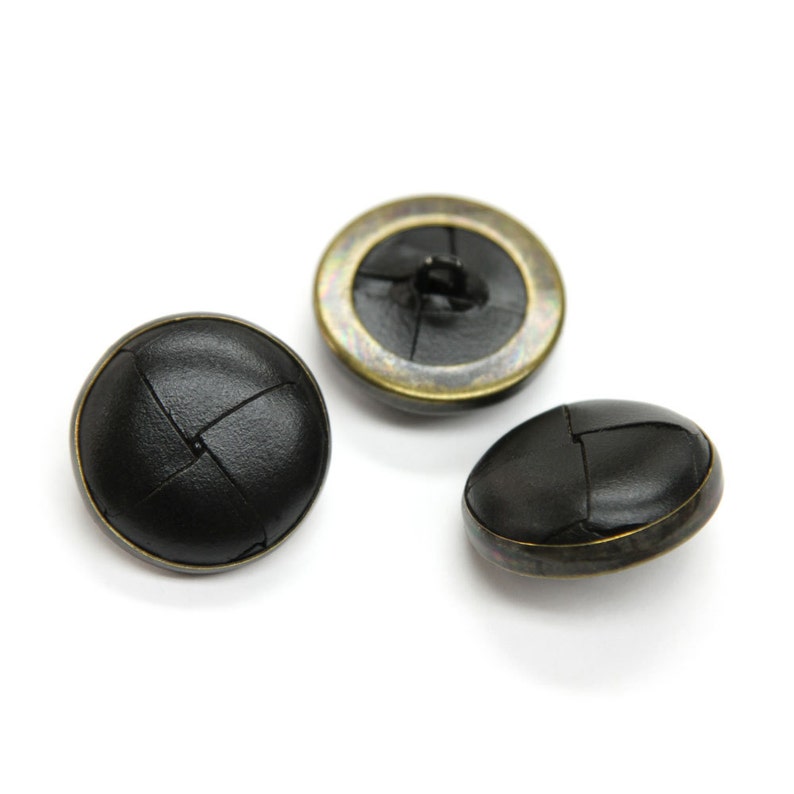 May include: Three black leather buttons with a gold metal rim. The buttons have a woven design.