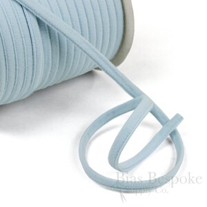 May include: A spool of light blue velvet bias tape. The tape is rolled up and a length of the tape is looped around the spool.