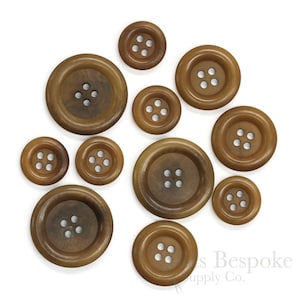 May include: A collection of brown wooden buttons of varying sizes, each with four holes. The buttons have a slightly rounded shape and a smooth, polished finish. The buttons are arranged on a white background.