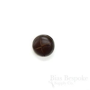 May include: A brown leather button with a cross-stitch design and a gold rim.