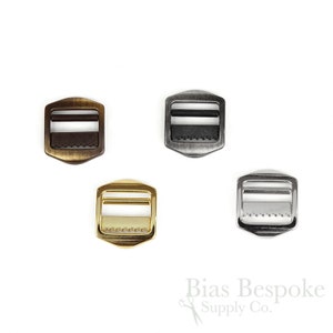 May include: Four metal slider buckles in different finishes: antique brass, nickel, gold, and silver. Each buckle has a rectangular shape with rounded corners and a center bar.