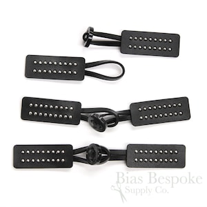 May include: Four black leather toggles with silver studs and black elastic loops. The toggles are in various sizes and are arranged in a row.