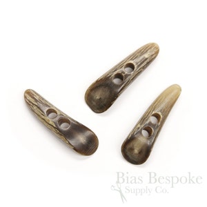 May include: Three brown horn toggle buttons with two holes each. The buttons are long and narrow with a rounded end.