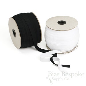 May include: Two spools of bias tape, one black and one white, sit on a white surface. The black tape is unrolled, revealing its texture. The white tape is neatly wound. The logo "Bias Bespoke Supply Co." is visible in the bottom right corner.