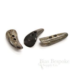 May include: Three brown and black horn buttons with two holes each. The buttons are shaped like a teardrop and have a natural wood grain pattern.
