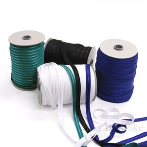 May include: Four spools of elastic ribbon with contrasting stripes. The spools are wound with teal, white, black, and blue ribbon.