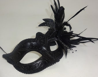 May include: A black masquerade mask with a delicate lace design and a black feather embellishment.