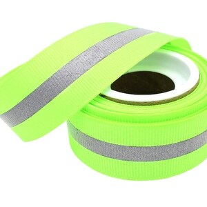 May include: A roll of lime green ribbon with a silver reflective stripe. The ribbon is rolled up and ready to be used for crafts, decorations, or other projects.