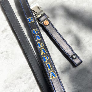 May include: A black leather strap with blue stitching and the word "GALAPIA" in gold lettering. The strap has a silver metal clip.