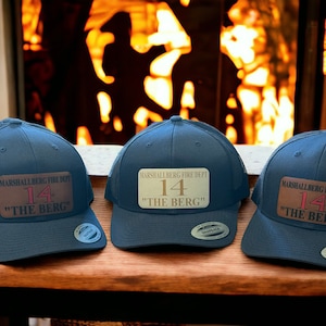 May include: Three blue and black mesh trucker hats with a brown patch that says "MARSHALLBERG FIRE DEPT" and "14" in red with the words "THE BERG" in white.