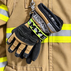 May include: A pair of tan and black firefighter gloves with a bright yellow reflective strap featuring the text MYE. The gloves are labeled FIRE KNIGHT and CROSSTECH, and are attached to a tan jacket with a metal clip and hook.