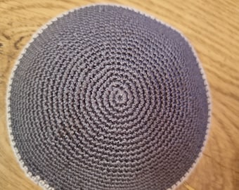 May include: A gray crocheted kippah with a white trim. The kippah is round and has a textured surface.