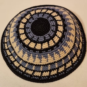 Può includere: Una kippah all'uncinetto con un motivo geometrico nero, blu e beige.