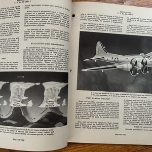 May include: An old aviation manual open at two pages. One page has a diagram of cloud formations and icing regions. The other page features a detailed drawing of a B-17 bomber, with text about flight safety.