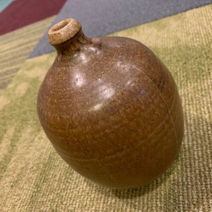 May include: A brown ceramic vase with a rounded body and a narrow neck. The vase has a textured surface and a glossy finish.