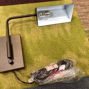 May include: A brown wall-mounted reading lamp with a white shade and a cord. The lamp has a flexible arm and a switch on the base.